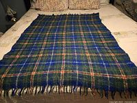 Full view of the vintage Nova Scotia Tartan blanket spread out on a bed, showing the classic green, blue, white and red plaid pattern and fringed edges.