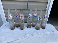 Group of seven empty swirl-pattern Pepsi bottles on towel