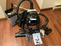 Full view of canister vacuum, hose, wand, accessories, bags box and manuals