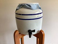 Front view of ceramic crock with blue stripes and spigot on wooden stand