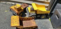 Photo showing two vintage Tonka metal dump trucks side by side outdoors on concrete.