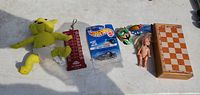 Photo showing all items: plush cat toy, cribbage scorer, Hot Wheels car, two masks, doll, wooden chess/checkers board.