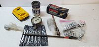 Photo showing yellow battery charger pack, combination wrenches, Bosch drill bits, pressure gauge, various sockets, valve sander accessory with extension bar on white surface.