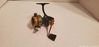 Black and gold fishing reel side view showing handle and spool.