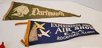 Green Dartmouth felt pennant with Native American chief profile and Dartmouth text paired with blue Experimental Aircraft Air Show pennant from Rockford, Illinois with airplane graphics