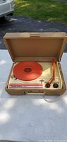 Front view of Fisher Price record player showing orange turntable and tonearm inside beige carrying case.