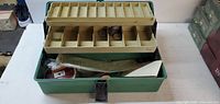 Green tackle box open showing beige compartment tray with fishing weights and various tackle inside box