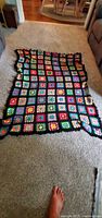 Photo of the large handmade afghan blanket laid flat on carpet, showing colorful crochet granny squares with black borders.