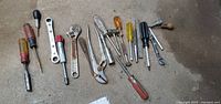 Photo showing full assortment of metal hand tools, including screwdrivers with various handle colors, adjustable wrench, pliers, and ratchets.