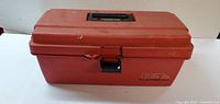 Red plastic Flambeau tool box with handle and latch, closed, sitting on flat surface against white background.