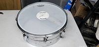 Silver snare drum showing Remo clear batter head with some wear marks and drum shell with chrome hardware.