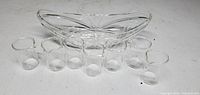 Lot of six small glass beakers and one glass candy dish on white surface