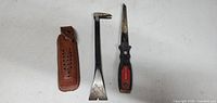 Photo of three small hand tools: leather sheath, flat pry bar, saw blade with handle.