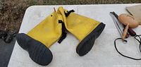 Pair of yellow and black rubber boots laid flat showing soles and straps