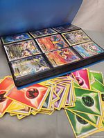 Binder open showing holographic EX/V cards in sleeves with loose energy cards in foreground