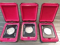 All three coins in open red display cases