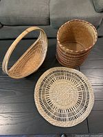 Group shot of all three wicker/rattan items: handled oval basket, cylindrical basket, round placemat