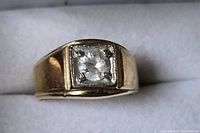 Top view of gold-plated men’s ring showing square bezel and clear stone