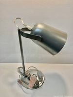 Side view of brushed silver lamp showing tilting conical head, stem, base, cord and plug