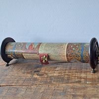 Closed scroll-shaped wooden pen case showing decorative manuscript motif and end feet