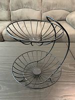 Full view of black two-tier wire fruit basket stand showing spiral support and both baskets