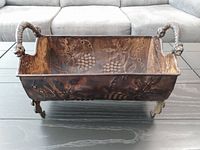 Front view of rectangular metal planter showing embossed grapevine design, ornate handles and feet