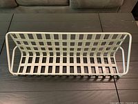 Top front view of off-white metal wall basket shelf showing grid back, base, and rounded sides