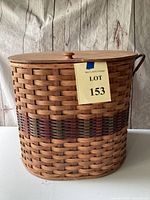 Full front view of the oval wicker basket showing woven design with darker accent bands and fitted wood lid with knob.