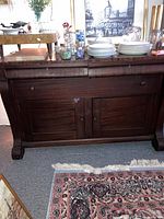 Front view of antique mahogany sideboard showing drawers and cabinet doors with staging items on top.