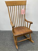 Front view of antique Windsor style wooden rocking chair showing spindle back and curved arms, surface wear on seat and rockers visible.