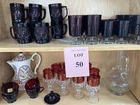 Two images of the same shelving area showing vintage glassware collection and porcelain coffee pot, including mugs, goblets, decanter and serving pieces