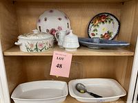 Shelf display of assorted vintage ceramic and glass servingware including floral casserole with lid, white serving dishes, and plates with floral patterns