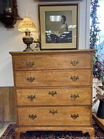 Front view of an oak antique chest of drawers showing four drawers with ornate brass hardware and warm wood with a smooth patina.