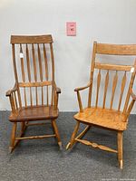 Front view of both antique wooden rocking chairs showing their spindle backs and armrests with natural wood finish.