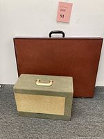 Two carrying cases pictured, one larger brown/red hard case and one smaller green/grey fabric-covered case with handle