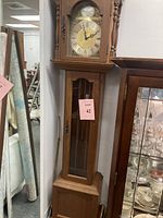 Full view of the Emperor grandfather clock in wooden casing with glass door showing pendulum and weights along with the clock face on top.