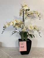 Full view of faux orchid plant showing multiple white blooms and green leaves in black pot