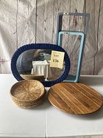 Full set showing six woven wicker plates stacked, round wooden cutting board, oval mirror with blue wicker-like frame, and two rectangular wall shelves in blue tones.