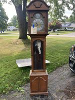 Full view of tall wooden grandfather clock showing traditional design, wood grain finish and overall condition.