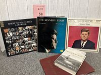 Five Kennedy memorabilia items including two vinyl albums, two hardcover books, and one red softcover book/album.