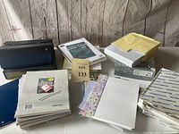 Assortment of stationery papers, letterhead packs, decorative stationery, and file folders stacked against a wood panel background