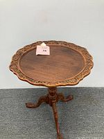 Full view of the carved wood pedestal side table, showing round top with carved decorative edge and clawfoot legs