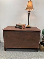 Front view of rectangular wooden blanket chest showing warm brown finish and simple design topped with lamp and books.