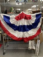 Set of three large red, white, and blue pleated fan buntings displayed on a metal shelving unit, showing the full size and colors of the bunting.