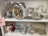 View of two shelves with porcelain figurines, serving tray, mirror, and various porcelain and glass items
