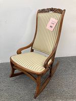 Rocking chair angled side view showing carved floral detail on top rail, gently curved armrest, and striped upholstery.