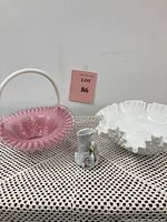 Three items displayed on crochet cloth. Pink and white glass basket, white ruffled milk glass bowl, and small floral vase are visible.