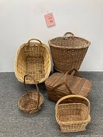 Front view of five woven baskets varying in size and shape including large gathering baskets, round lidded basket, picnic basket, and small handled baskets.
