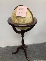 Full view of vintage floor globe mounted on wooden pedestal stand with tripod base.