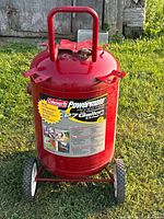Front view of red Coleman Powermate 27 gallon air compressor tank with label and handle visible, standing outdoors on grass.